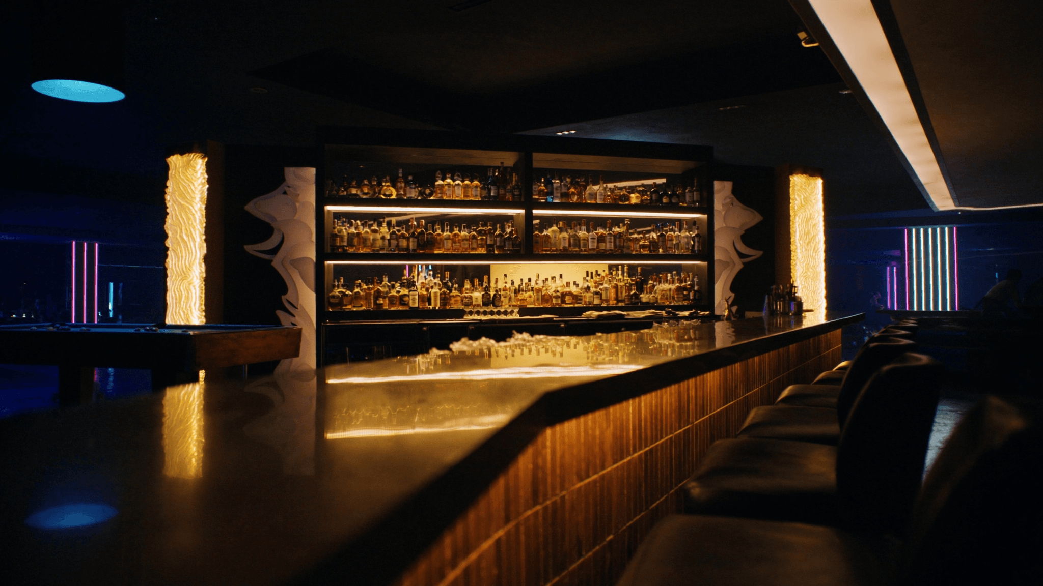 The NYX bar back-lit in warm amber, a polished counter mirroring rows of premium bottles.