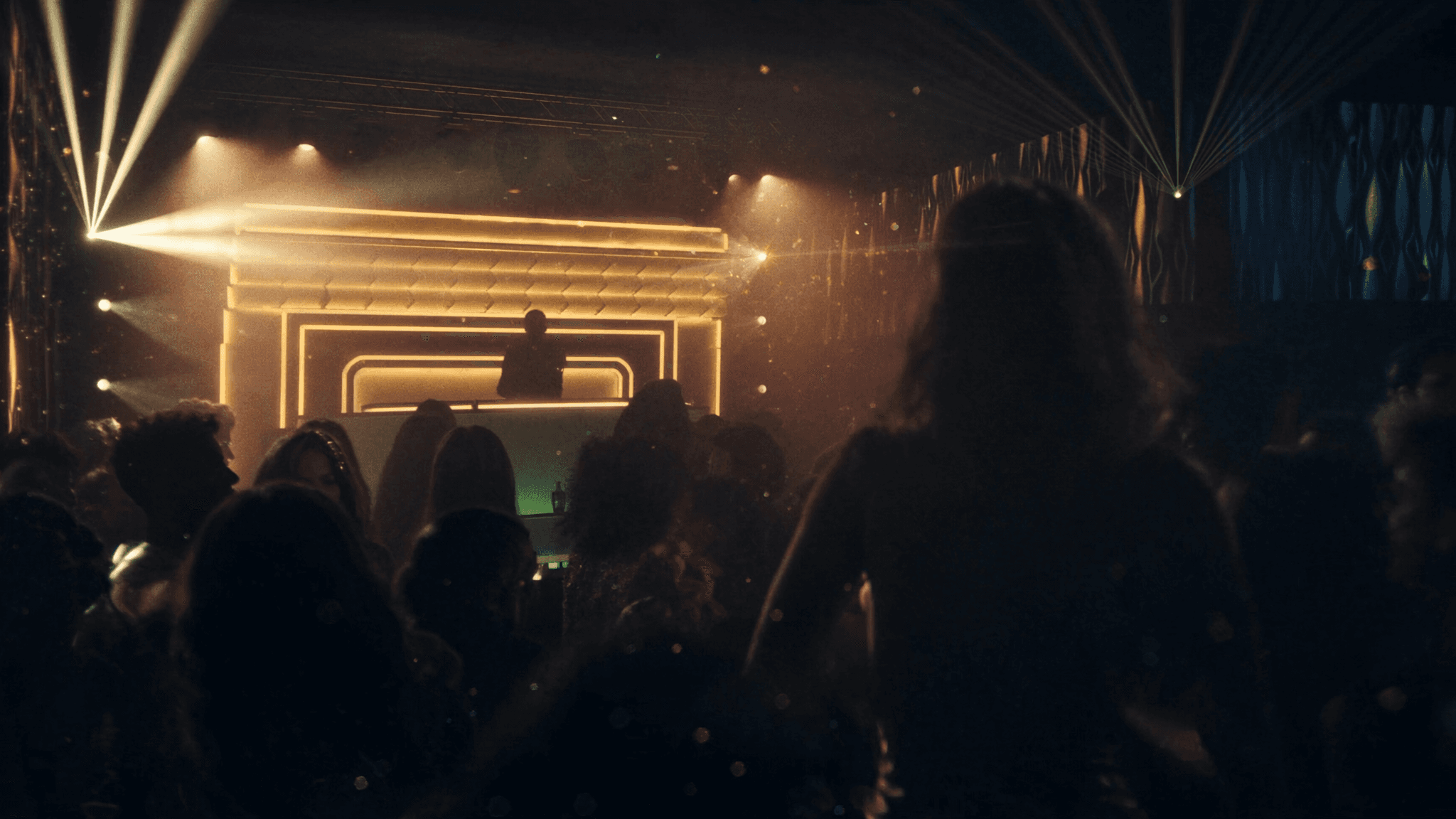 The NYX main floor at night — golden DJ-booth glow over a packed dancefloor, light beams cutting through haze.