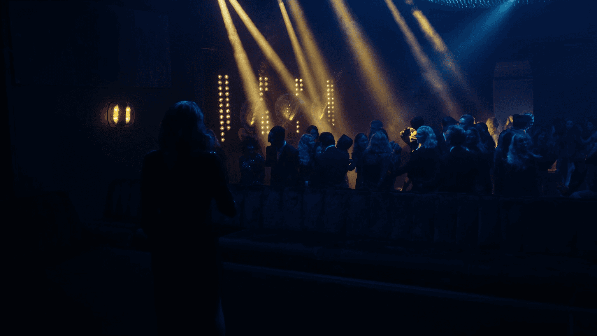 Stage spotlights fanning across the NYX floor in gold and blue beams through atmospheric haze.